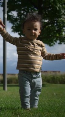 Neşeli bir çocuk, enerji dolu, bir parkı keşfeder, güneşli bir günün tadını çıkarırken erken yürüyüş becerilerini sergiler.