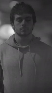 Rahat bir kapüşonlu giyen genç bir adam gözleri kapalı oturur. Huzurlu ve huzurlu bir atmosferi derinden yansıtır.