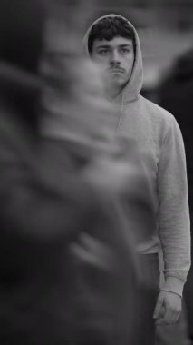 Gri kapüşonlu genç bir adam canlı bir şehir arkaplanına karşı güvenle duruyor, sakinlik saçıyor.