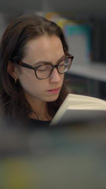 Bir kadın yoğun bir şekilde çağdaş bir çalışma alanı içinde kitap okumaya odaklanır ve dikkate değer bir konsantrasyon gösterir.