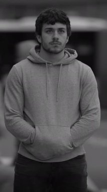 Genç bir adam düşünceli bir duruş sergiliyor, elleri ceplerine konmuş, derin bir düşünce yayıyor.