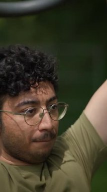 Gözlüklü genç bir adam dışarıda egzersiz yapıyor, sıkı antrenmanlarla spor ve dayanıklılığı geliştirmeye odaklanmış.