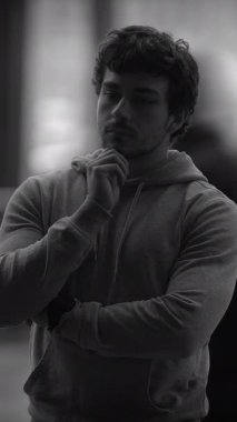 Sıradan bir kapüşonlu giyen düşünceli genç bir adam derin derin düşüncelere dalıp derin bir duruş sergiliyor.