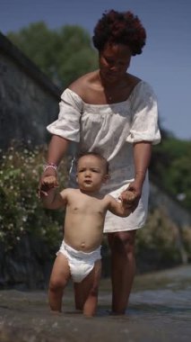 Neşeli bir anne bebeğini sığ sularda nazikçe yönlendirir. Güzel bir bağ ve sevgi anını yakalar.