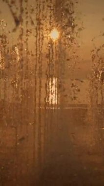 Zarif su çeşmeleriyle çerçevelenmiş nefes kesici altın bir günbatımı derin bir huzur ve sükunet hissi uyandırıyor.