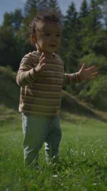 Neşeli ve neşeli bir çocuk dışarıda oynuyor, yemyeşil bir tarlada güneşli güzel bir günde el çırpıyor.