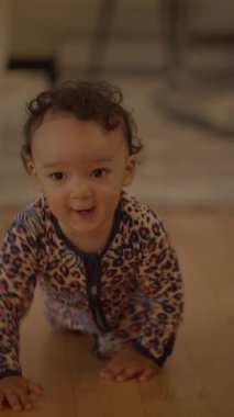 Sevimli bir leopar desenli tulumun içinde mutlu ve neşeli bir bebek sıcak ahşap zeminde mutlu bir şekilde sürünüyor.