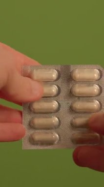 Yakından çekilen bir resim, canlı yeşil bir arkaplana karşı renkli kapsüllerden oluşan su toplayan bir el görüntüsü yakalar.