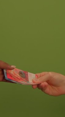 Finansal işlemleri sembolize eden canlı yeşil bir arka plana karşı bir el renkli bir banknot sunuyor.