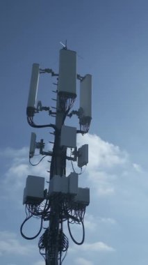 Çok yüksek bir hücresel kule belirgin bir şekilde açık mavi gökyüzünün altında çeşitli anten ve ekipmanları sergiliyor.