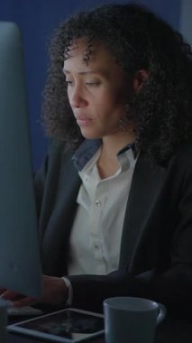 Kendini işine adamış ve çalışkan bir kadın, loş bir ofis ortamında özenle bilgisayar üzerinde çalışıyor.