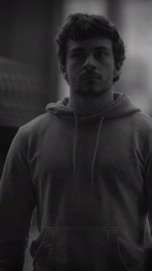 Şık bir kapüşonlu giyen odaklanmış genç bir adam kendine güvenen, kararlı ve güçlü bir şekilde ayakta duruyor.