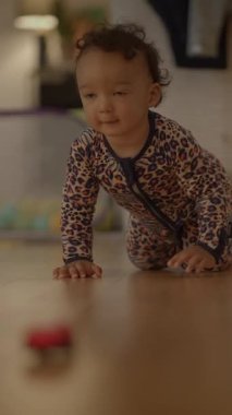 Meraklı, çekici, leopar desenli tulum giymiş bir çocuk heyecanlı bir şekilde küçük kırmızı bir oyuncak arabaya doğru sürünüyor.