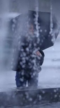 Israrlı yağmur ve bulanık su damlaları arasında parlak bir şemsiye tutan yalnız bir insanın çarpıcı silueti.