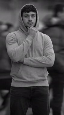 Şık bir kapüşonlu giysili genç bir adam canlı bir açık hava sahnesini izlerken düşünceli bir şekilde yansıtır