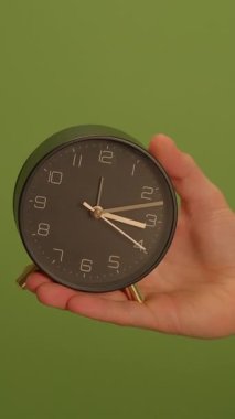Şık ve modern bir çalar saat, canlı yeşil bir arka plana karşı bir elde sunulur, güzelce sergilenir.