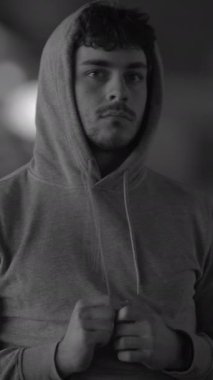 Siyah beyaz bir portre, derin bir tefekkür içinde şık bir kapüşonlu giyen genç bir adamı gösteriyor.