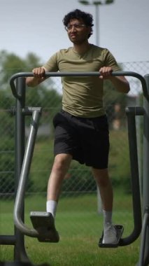 Genç bir adam, bir park ortamında bulunan spor aletlerini kullanırken aktif olarak dışarıda egzersiz yapıyor.