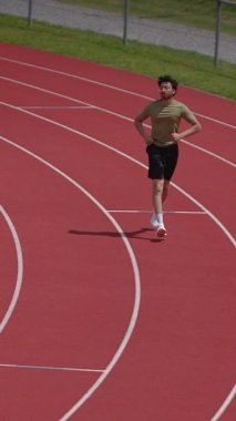 Kendini adamış ve tutkulu bir atlet, açık güneşli havanın altında canlı kırmızı bir pistte sıkı çalışıyor.