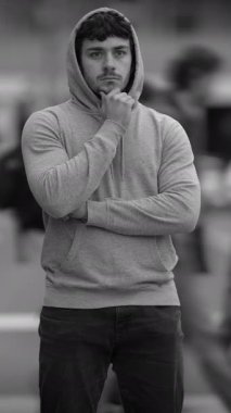 Kapüşonlu genç bir adam derin düşüncelere dalmış, bulanık bir şehir geçmişiyle kasvetli bir atmosfer yaratıyor.