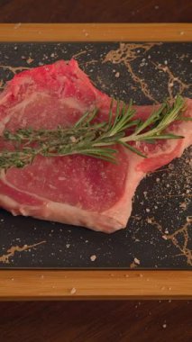 Güzel sunulmuş, aromatik taze biberiyeyle süslenmiş çiğ bir biftek şık bir tahta üzerinde zarif bir şekilde oturur.