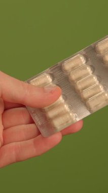 Bir el, parlak yeşil bir arkaplan üzerine kurulmuş renkli kapsüllerle dolu bir su toplayıcı paketini sıkıca kavrıyor.