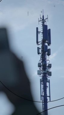 Çağdaş bir telekomünikasyon kulesi antenlerle süslenmiş ve yukarıdaki parlak mavi gökyüzüne kadar uzanıyor.