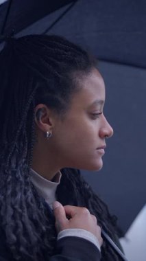 Düşünceli bir kadın, yağmurlu bir şehir ortamının ortasında, bir şemsiyeyle sessizce korunuyor.