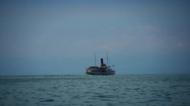 Eski bir gemi bulutlu ve kasvetli bir gökyüzünün altında durgun sularda süzülerek huzur verici bir manzara yaratıyor.