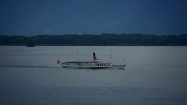 Resimli bir vapur, arka plandaki görkemli dağların altında huzurlu sularda sorunsuzca süzülüyor.