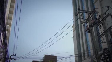 Açık mavi gökyüzü altında çağdaş binaların zeminine kurulmuş çoklu elektrik hatlarının ele geçirilmesi