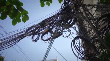 Açık mavi gökyüzünün altında hareketli bir şehir şehrinde karmaşık ve karmaşık renkli elektrik kabloları ve kablolar.