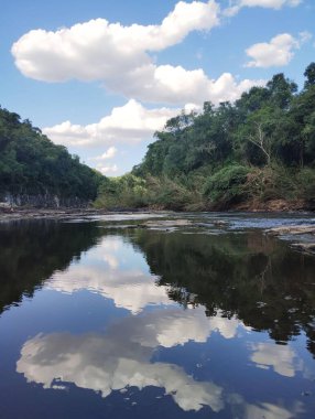 Bulutların yansıdığı mavi gökyüzü, sıcak ve güneşli bir yaz gününde, doğanın ortasındaki bir nehrin kristal berrak suyuna yansıyor. Sessiz, sakin ve huzur dolu.