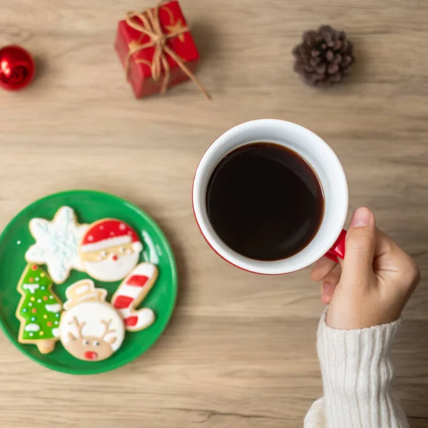 Merry Christmas with woman hand holding coffee cup and homemade cookie on table. Xmas eve, party, holiday and happy New Year concept