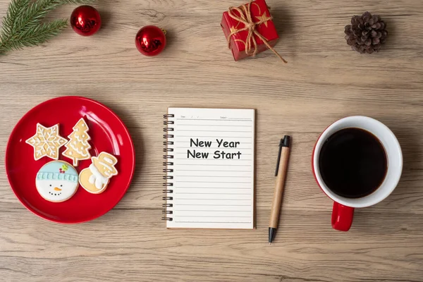 New Year New Start with notebook, black coffee cup, Christmas cookies and pen on wood table.  Xmas, Goals, Resolution, To do list, Strategy and Plan concept
