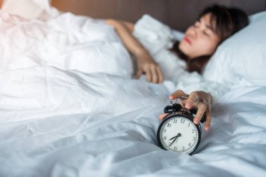 Çalar saat ve Asyalı kadın el, uyurken zamanı durdurur. Yetişkin genç dişi, sabah geç saatte uyanır. Rahatlatıcı, uykulu, günlük rutin ve iyi günler.