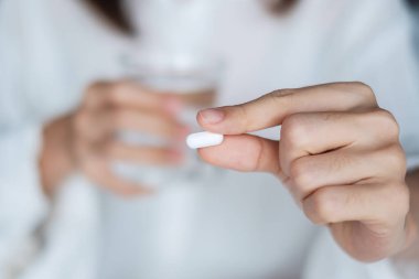 Yetişkin bir kadın elinde hap ve bir bardak su tutuyordu. Kadın evde yatağında ilaç alıyordu. Migren, ağrı kesici, baş ağrısı, grip, hastalık, hastalık ve sağlık sigortası kavramı
