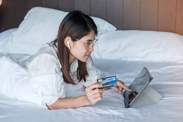 woman using tablet and credit card for online shopping while making order on bed in morning at home. technology, ecommerce, digital banking online payment and apartment living concept