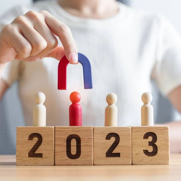 stock image hand holding magnet and pulling man wooden figure from the crowd employee with 2023 Year block. Human resource management, Recruitment, Teamwork, strategy, toxic people and leadership Concepts