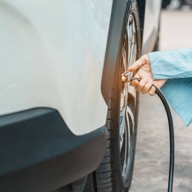 woman driver hand inflating tires of vehicle, removing tire valve nitrogen cap for checking air pressure and filling air on car wheel at gas station. self service, maintenance and safety