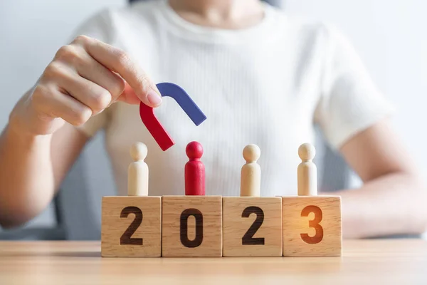 stock image hand holding magnet and pulling man wooden figure from the crowd employee with 2023 Year block. Human resource management, Recruitment, Teamwork, strategy, toxic people and leadership Concepts