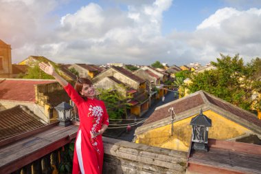 Ao Dai Vietnamlı elbisesi giyen mutlu bir kadın Hoi An antik kasabasının çatı katını gezen gezgin manzarası. Tarihi bir yer ve turistik yerlerin gözdesi. Vietnam ve Güneydoğu seyahat kavramı