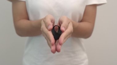 Melanoma ve cilt kanseri için siyah kurdele tutan kadın, Aşı yaralanması farkındalığı ayı, keder ve huzur içinde yatsın. Sağlık ve Irkçılık Konsepti