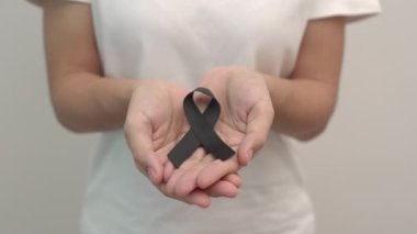 Melanoma ve cilt kanseri için siyah kurdele tutan kadın, Aşı yaralanması farkındalığı ayı, keder ve huzur içinde yatsın. Sağlık ve Irkçılık Konsepti