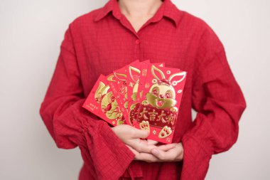 Woman holding Chinese red envelope with golden rabbit and blessing word, money gift for happy Lunar New Year holiday. Chinese sentence means happiness, healthy, Lucky and Wealthy