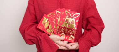 Woman holding Chinese red envelope with golden rabbit and blessing word, money gift for happy Lunar New Year holiday. Chinese sentence means happiness, healthy, Lucky and Wealthy