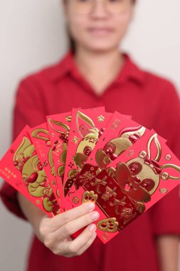 Woman holding Chinese red envelope with golden rabbit and blessing word, money gift for happy Lunar New Year holiday. Chinese sentence means happiness, healthy, Lucky and Wealthy