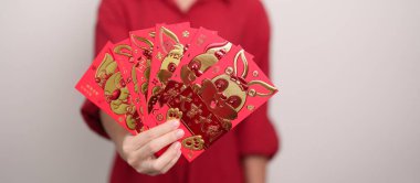 Woman holding Chinese red envelope with golden rabbit and blessing word, money gift for happy Lunar New Year holiday. Chinese sentence means happiness, healthy, Lucky and Wealthy