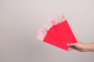 Woman holding Chinese red envelope with Thai baht money gift for happy Lunar New Year holiday