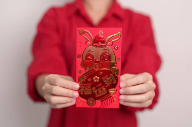 woman holding Chinese red envelope with golden rabbit and blessing word, money gift for happy Lunar New Year holiday. Chinese sentence means happiness, healthy, Lucky and Wealthy